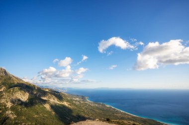 Dağlarda güneşli bir gün, dağ zirveleri, mavi gökyüzü, dağların tepelerinde bulutlar, kayalar, keskin zirveler ve dik yamaçlar..