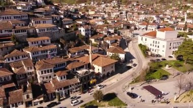 Arnavutluk 'un Berat kentindeki evler, camiler ve minarelerden oluşan kiremitli çatıların üzerinden uçuyorlar. Arnavutluk 'un en güzel kenti Berat' taki muhteşem Osmanlı binaları. Hava görüntüsü, 4K