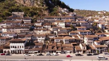 Flying over tiled roofs of houses, mosques and minarets in Berat, Albania. Magnificent Ottoman buildings in the most beautiful city of Albania - Berat. Aerial view, 4K