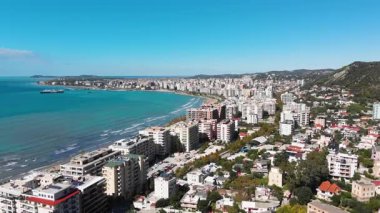 Arnavutluk 'un Vlora kenti yakınlarındaki çarpıcı Riviera kıyı şeridinin insansız hava aracı görüntüsü, Saranda' da el değmemiş beyaz plajlar, turkuaz deniz suyu, kayalıklar ve Akdeniz güneşinin altındaki dağlar görülüyor.