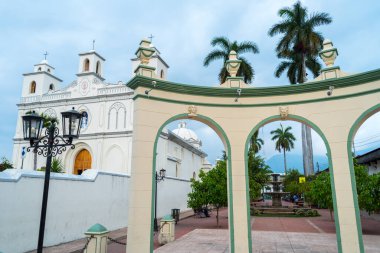 Pasaje La Concordia Ahuachapn El Salvador 'daki dekoratif bir kemerin yanında ikiz çan kuleleri olan beyaz bir koloni kilisesi duruyor..