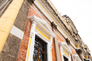 Quetzaltenango, Guatemala 'da tarihi bir binanın ön cephesinde koloni tarzı mimari yer alıyor. Görüntü, kentin mimari mirasını gözler önüne seren sütunlar, işlenmiş demirden yapılmış pencereler, süslü detaylar ve ortaya konmuş tuğla çalışmalarını ön plana çıkarıyor..