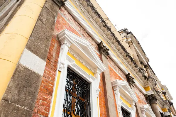 Quetzaltenango, Guatemala 'da tarihi bir binanın ön cephesinde koloni tarzı mimari yer alıyor. Görüntü, kentin mimari mirasını gözler önüne seren sütunlar, işlenmiş demirden yapılmış pencereler, süslü detaylar ve ortaya konmuş tuğla çalışmalarını ön plana çıkarıyor..