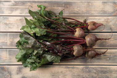 Soluk ahşap masa üzerinde uzun yeşil çekimli taze pancar demeti, üst manzara. Soyulmamış pancar köklerini pişirmeye hazırlayın. Organik gıda ya da sağlıklı diyet konsepti. Nesne düzeni. Planking.