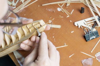 Geminin modelinin detaylarını kontrplaktan kesen adamın elleri. Oyuncak gemi, hobi ve el işi yapma süreci. İş için çeşitli materyal, parça ve aygıtlara sahip tablo