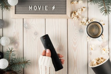 Uzaktan kumandalı rahat kazaklı kadın elleri, isim levhası filmi, bir fincan kahve, dekoratif kostüm ahşap arka planında patlamış mısır. Hafta sonu televizyon etkinliği, rahatla. Üst görünüm