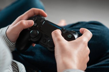 Evde oturan, elinde siyah oyun kumandası olan oyun konsolunda video oyunları oynayan tanınmamış bir genç çocuk. Hobi, boş zaman, oyun, eğlence, boş zaman. Yumuşak odak.