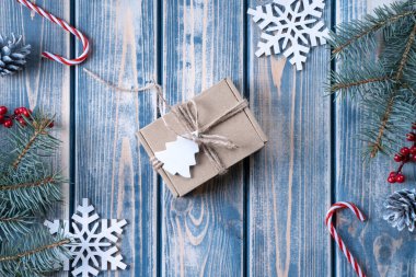 Kraft karton hediye kutusu. Gri ahşap arka planda kaba halatla bağlanmış. Noel ağacı dalları ve Noel süslemeleri var. Üst görünüm