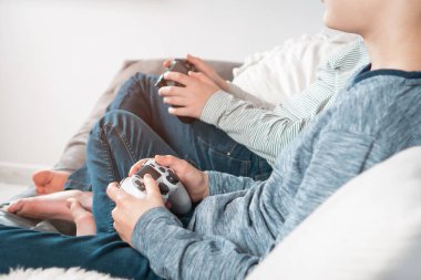 İki gencin evde oturup oyun kumandalı joystick oyun sahası tutarken konsol istasyonunda video oyunları oynarken çekilmiş bir fotoğrafı. Hobi, boş zaman, oyun, eğlence, arkadaşlık. Yan görünüm.
