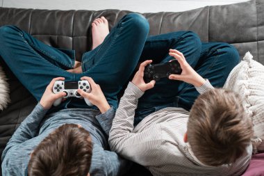 Evde gri kanepede oturan iki genç çocuğun oyun kumandalı joystick 'i tutarken video oyunları oynarken, eğlenirken en iyi görüntüsü. Hobi, boş zaman, oyun, eğlence, eğlence, arkadaşlık.