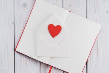 Kırmızı günlük defteri, beyaz kağıt, kırmızı kalp, el işi zarf içinde, ahşap masa arkasında. Aşk mektubu, mesaj yolluyorum. Sevgililer gününde ya da 8 Mart 'ta aşık olmak. Uzayı kopyala, düz yat
