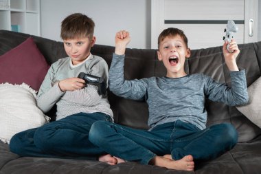 Kazanıp kaybetmekten farklı duygular. Okul çağındaki çocuklar ellerinde joysticklerle kanepede otururlar. Çocuklar video oyunları oynarlar. Çocuklar evde birlikte eğleniyor. Oyun yarışması. En iyi arkadaşlar yaşam tarzı.