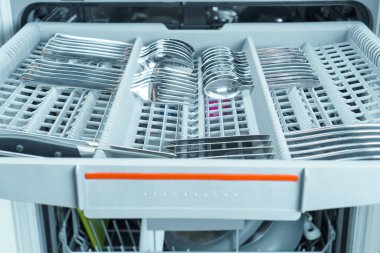 Üst kattaki bulaşık makinesinin bölmeleri temiz, parlak çatal bıçaklarla dolu. Bulaşık, kaşık, çatal, bıçak, modern ev aletleri. Çatal bıçak temizliği. Kullanışlı mutfak ekipmanları.