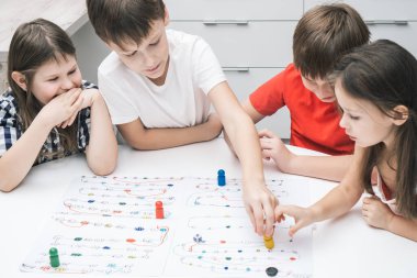 Beyaz masada oturan, masa üstü masa oyunu oynayan, beyaz tahtada rakamları ve rayları olan renkli figürleri hareket ettiren bir grup çocuk arkadaş grubu. Masa oyunları, eğlence.