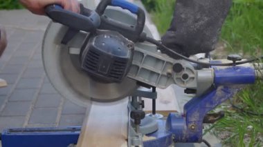 Tanımlanamayan marangoz elle itiyor ve dışarıdaki tahtaları kesmek için makinenin teknik dairesel testeresini kullanıyor. Havaya püsküren toz gördüm. Sokakta kalasları ayırmak. Görüntü tam Hd