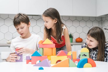 Mutlu okul arkadaşları mutfak masasında oyuncakçılık oynarlar. Kızlar lego hakkında renkli detaylar toplayan oğlanlara bakar. Küçük çocuklar oyuncak şehir inşa eder. Ev eğlencesi, oyun zamanı. Eğitici ilginç tahta oyunu.