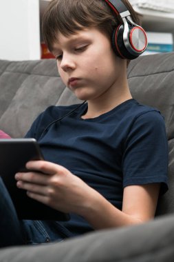 Dikey sükunet, kulaklıklı küçük bir çocuk müzik dinler ve dijital tabletli filmler izler, elinde ped, koltukta oturur. Taşınabilir Bluetooth aygıtı. Kulaklıklarınızda podcast 'ler.