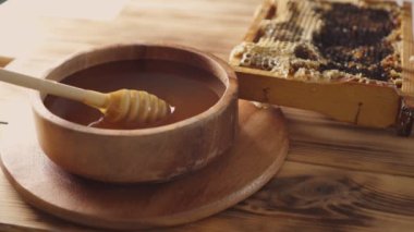 Arı kovanının yanında, masada bal petekleri olan yuvarlak tabakta lezzetli bal dolu ahşap kaseye yakın çekim. Tahta kaşık kapağından bal akıyor. Arıcılık, apikülcülük, arı yetiştiriciliği, tatlı..