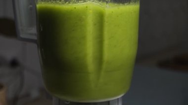Çalışan elektrikli mikserin yan görüntüsü taze yeşil meyve püresi hazırlıyor. Mutfak aletleri, sebzeler, meyveler, vejetaryen, sağlıklı yiyecekler, kahvaltı diyeti, yemek pişirme, detoks, vitaminler, içecekler..