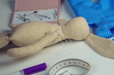 Masada iğneli oyuncak tavşan dolması dikmek. Örgü hobisi. Tavşan oyuncağı mavi benekli tekstil, mezura ve işaretin yanında. Oyuncakçı, dükkan. DIY, çocuklar burada