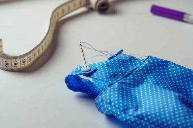 Küçük şirin, mavi benekli bir kostüm giymeye başladı. Oyuncak tulumları, mezura ve beyaz masa üzerindeki kalemle birlikte. Oyuncak ve giysi dikme süreci. Örgü hobisi. DIY, çocuk mağazası