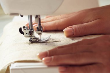 Tanımlanamayan kadın terzi elleri dikiş makinesinin iğne desenli dikiş desenine dikişli beyaz yumuşak kumaş tekstil döşüyorlar. Atölyede kıyafet üretimi