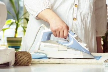 Beyaz gömlekli, buharlı, mavi buruşuk kumaşlı, beyaz gömlekli bir kadın. Terziler kumaşı dikmek için hazırlar, içeride imalat yaparlar. Küçük işletme ya da hobi. Kapat.