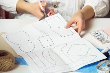 Kadın tasarımcı ellerinin kesilmiş görüntüsü kağıt çarşaflardan desenler keserek kıyafet ve oyuncaklar yapıyor. El işi ve dikiş işi. Üretim atölyede ve atölyede çalışıyor.