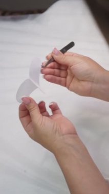 Beyefendinin beyaz leke çıkartmasını cımbızla çıkardığı ve parmağına ince sarkıtılan ellerinin videosu. Kadın kirletici, müşterinin göz kapağına malzeme uygulamaya hazırlanıyor. Dikey.