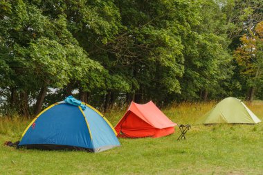Mavi, kırmızı ve açık yeşil renkli üç ahır çadırı yaprakların önündeki çimlerin üzerine kurulmuş heyecan ve sükunetle dolu unutulmaz bir macera vaat ediyorlar..