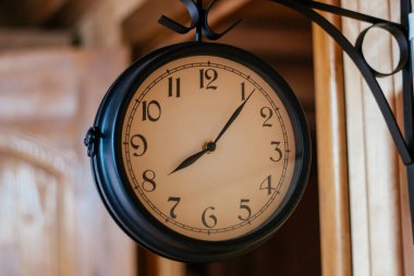 Köşe başındaki tahta duvarda asılı siyah metalden yapılmış yuvarlak bir saat. Dekoratif elementler. Geri sayım. Tasarım. Retro tarzı. Zaman kavramı. Yuvarlak saat tabelası. Yuvarlak şekli oluştur.