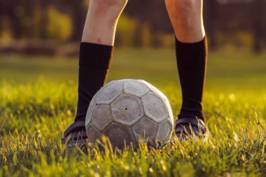 Yüksek çoraplı tanınmayan genç sporcu yaz sabahının erken saatlerinde biçilmiş çimlerin üzerinde futbol topunun önünde duruyor. Spor ve sağlık. Çocuk bölümleri. Futbol antrenmanı. Yaz sporları kampı. 