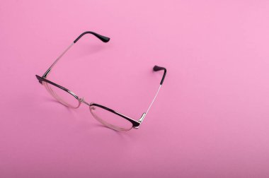 Siyah çerçeveli gözlük, pastel pembe arka planda izole edilmiş.