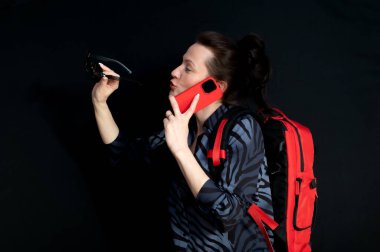  Güneş gözlüklü, kırmızı sırt çantalı, siyah arka planda konuşan genç ve güzel bir kadın.