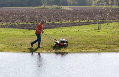 Orta yaşlı bir adamın güzel bir bahar akşamı gölette çimleri biçerken fotoğrafı..