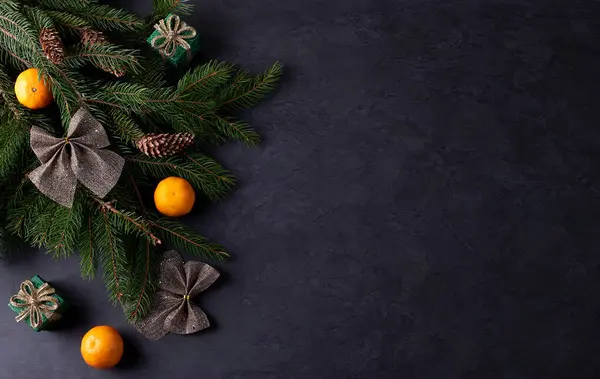 stock image Christmas decoration with fir branches, cones and tangerines on a dark background