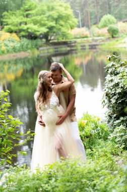 Mutlu hamile çift gölde birbirlerine sarılıyorlar.