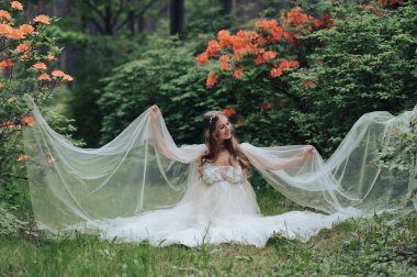 Romantik hamile kadın çiçek açan orman parkında lüks beyaz elbiseler giyiyor.