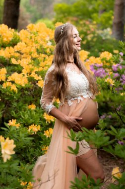 Rhododendron parkında duran hamile bir kadın. Doğanın çiçek açtığı hamile karnını kapat..