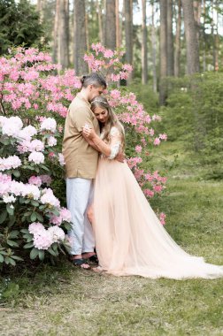 Çiçek bahçesinde kucaklaşan mutlu hamile çift. Çiçek açan rhododendron parkında müstakbel ebeveynler.