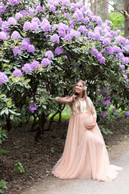 Romantik hamile kadın lüks elbiseler içinde çiçek açan bir orman parkında dans ediyor.