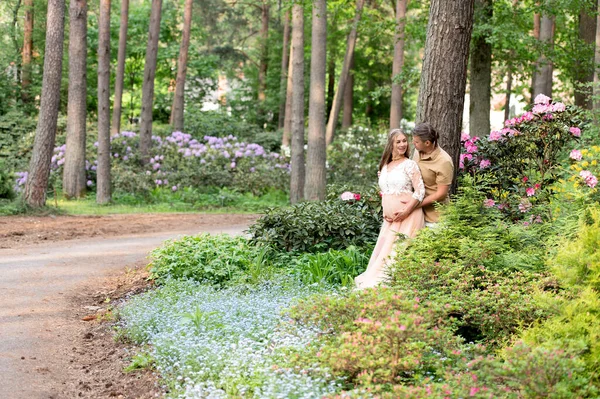 赫比怀孕的夫妇在花园子里拥抱 在盛开的杜鹃园 未来的父母 — 图库照片