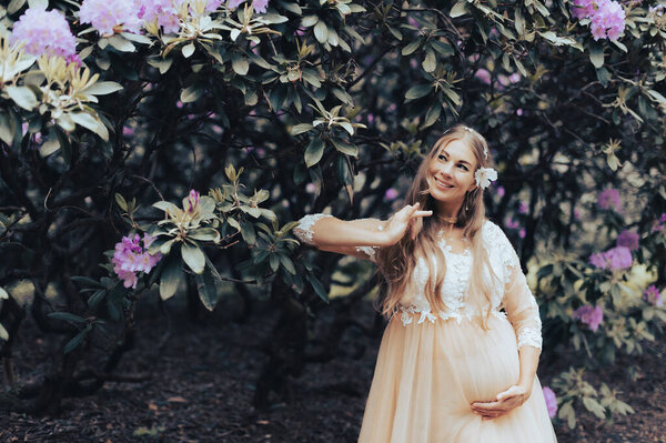 Romantic pregnant woman wearing luxury dress dancing in a blooming rhododendron park
