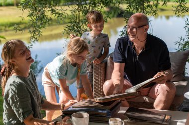 Grandpa with his grandchildren looking at old photo albums on outdoor terrace on a sunny summer day clipart