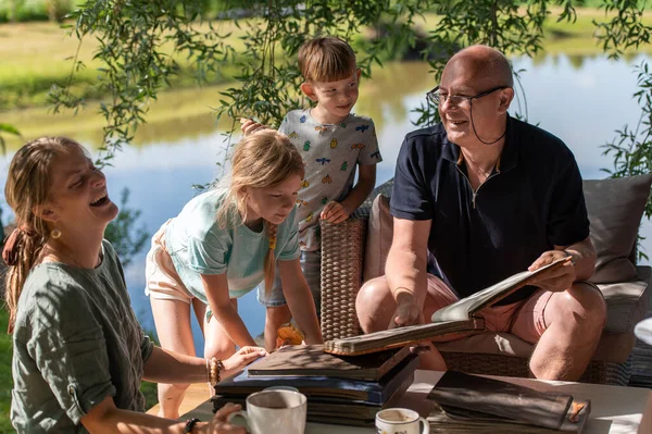 stock image Grandpa with his grandchildren looking at old photo albums on outdoor terrace on a sunny summer day