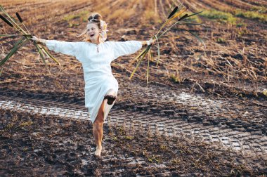 Çamurlu bir tarlada çıplak ayakla dans eden, elinde kamışlarla mutlu bir kadın.