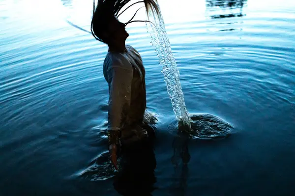 Woman splashing water with her hair in lake. Selective focus. Hair in motion blur.