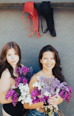 Gri arka planda sütyen altında çiçek açan leylakları olan iki seksi kadının komik çift portresi.