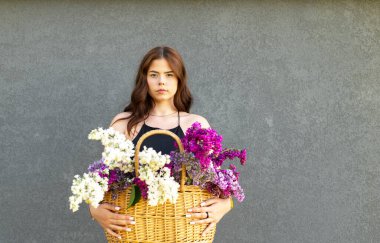 Şehvetli genç kız sepetini gri duvar arkasında izole edilmiş renkli leylak çiçekleriyle tut. 