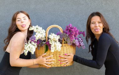 İki kadın leylak sepetini tutuyor ve neşeli bir ifade takınıyor. Ağzını açıyor ve dilini gösteriyor.